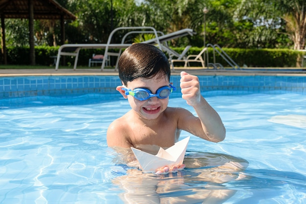 Niño en la piscina, con el puño cerrado, va a destruir el bote de papel.