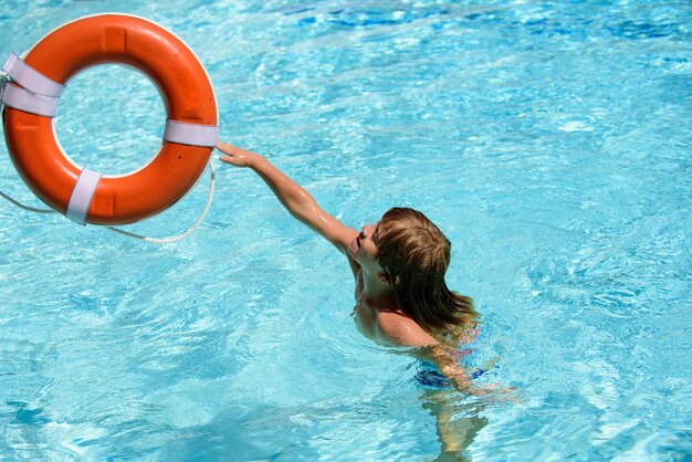 Niño en piscina de verano. Vacaciones de verano. Niño feliz en la fiesta en la piscina. Complejo de piscina. Anillo de rescate en piscina. Aro salvavidas naranja.