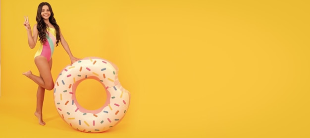 Niño de playa feliz en traje de baño con anillo inflable de donut sobre fondo amarillo Banner de niña de verano en traje de baño cabecera de cartel de estudio con espacio de copia