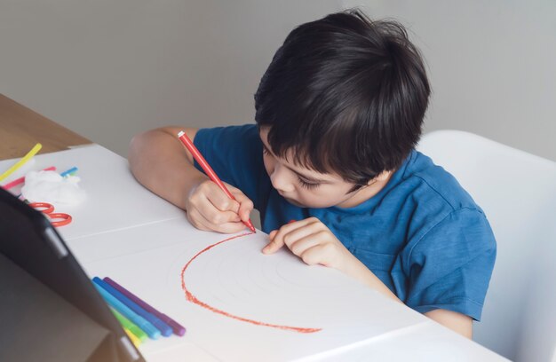 Niño con pluma roja para colorear arco iris sobre papel