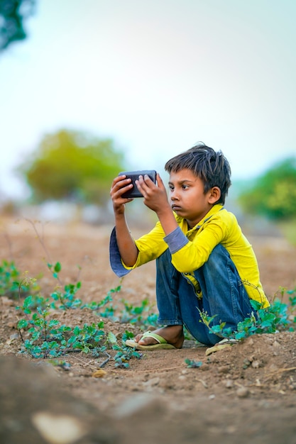 Niño pobre indio jugando con el móvil en el campo de la agricultura. Escena rural.