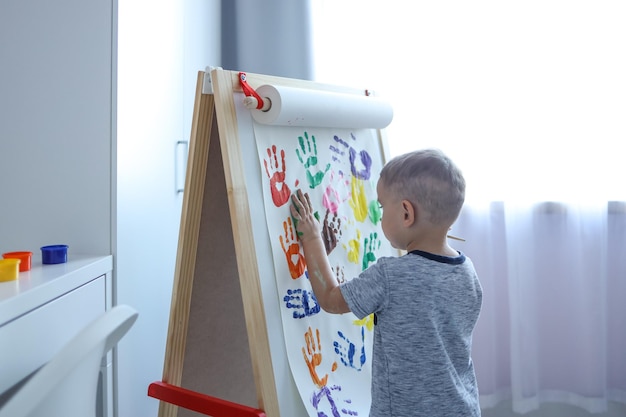 El niño pone huellas de manos con pinturas en el caballete el concepto de creatividad.