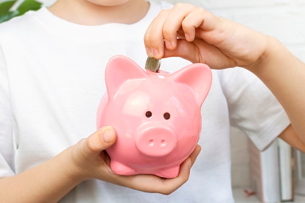 Foto un niño pone monedas en una alcancía rosa. responsabilidad financiera, acumulación, planificación de ahorros.