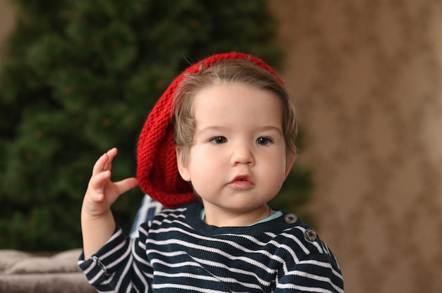 Un niño se pone un sombrero. Un sombrero rojo y un niño. muestra un dedo El niño tiene 0-1 años. Retrato de niño de un año.