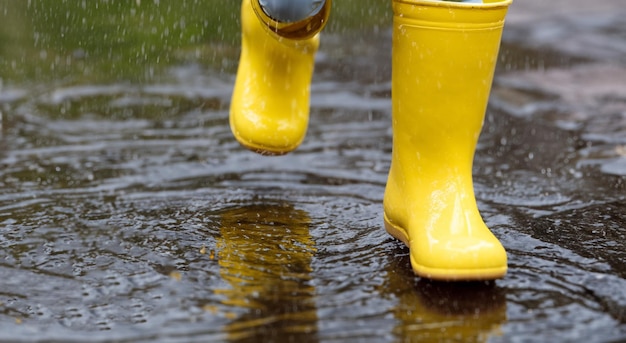 Foto niño poniendo botas amarillas en el charco