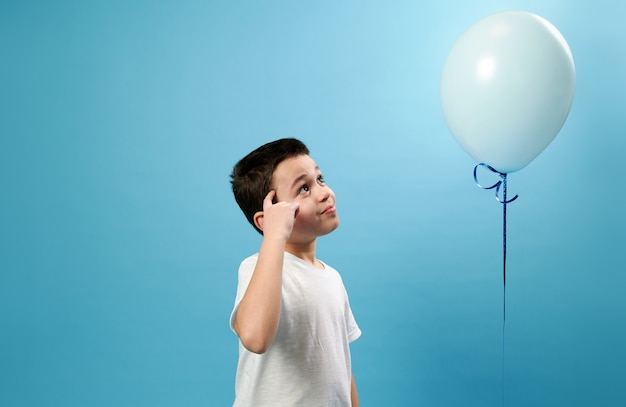 Niño poniendo su dedo en su sien y mirando el globo azul volador con una mirada pensativa