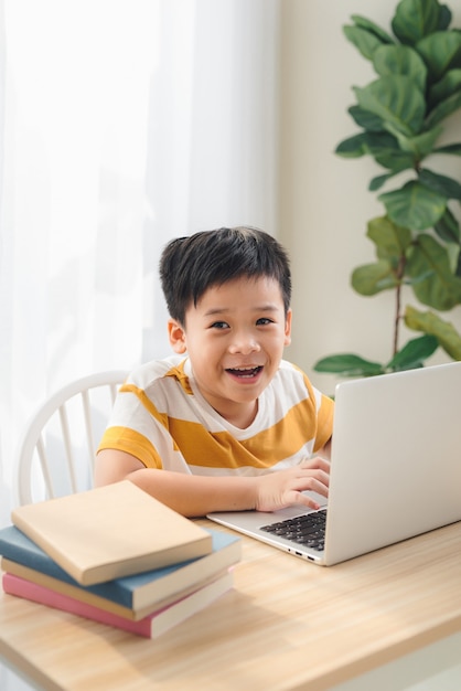 Niño preadolescente de Asia estudiando en línea en una computadora portátil con cara sonriente y divertida en casa. concepto de educación en línea y e-learning.