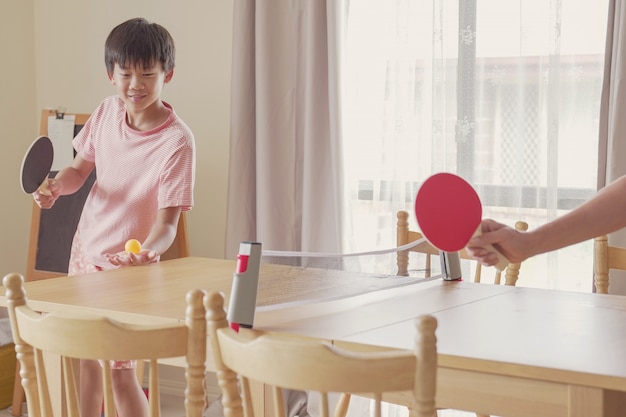 Niño preadolescente asiático mixto saludable jugando tenis de mesa en la mesa de comedor en casa, ejercicio de interpolación, fitness infantil, mantenerse saludable y en forma durante el distanciamiento social, concepto de aislamiento