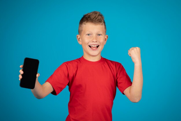 Niño preadolescente emocionado demostrando teléfono inteligente con pantalla negra en blanco en la cámara