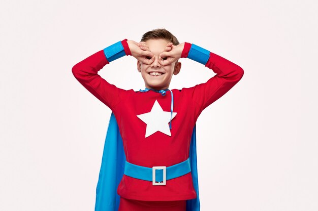 Niño preadolescente emocionado en traje de superhéroe haciendo gesto de búho