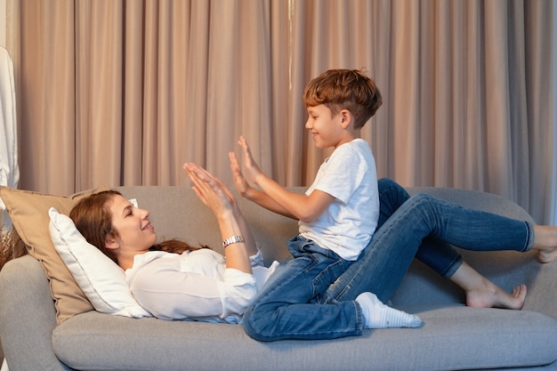 Niño preadolescente jugando con su madre en casa en el sofá