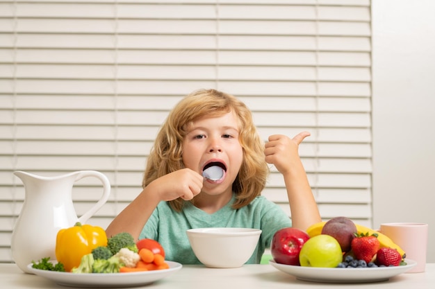 Niño preadolescente niño lamer cuchara en la cocina en la mesa comiendo verduras y frutas durante la cena