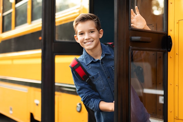 Foto niño preadolescente parado en la puerta del autobús escolar y mirando a la cámara