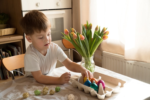 Niño preescolar caucásico jugando con coloridos huevos de Pascua en casa