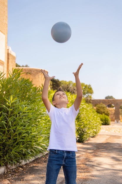 Niño preescolar feliz en camiseta blanca sosteniendo la bola al aire libre