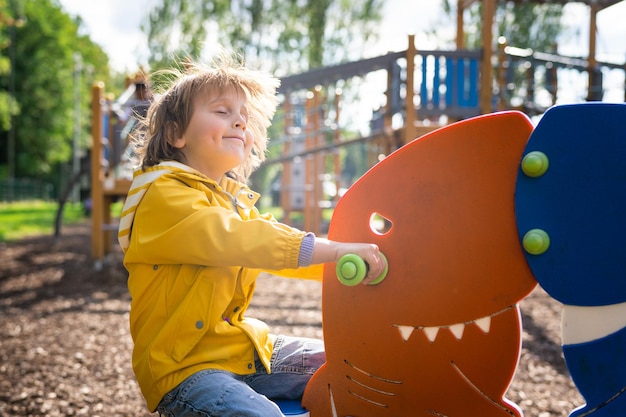 Niño preescolar en el patio de recreo para niños feliz niño emocional columpiándose en un tablero en un parque Concepto de infancia