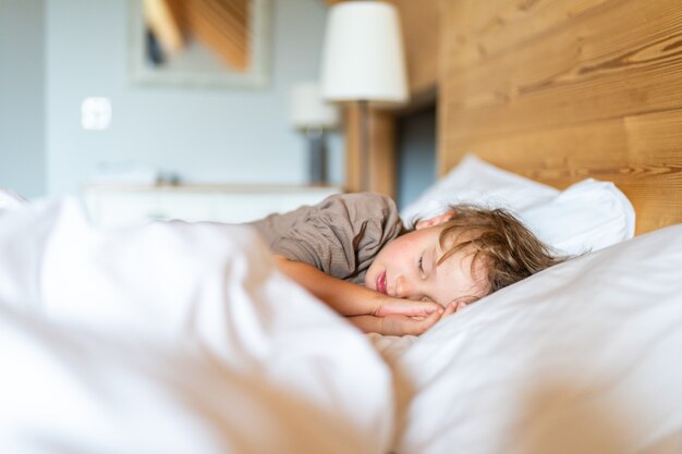 Niño preescolar en pijama está durmiendo en la cama en casa. El niño no quiere despertarse por la mañana.