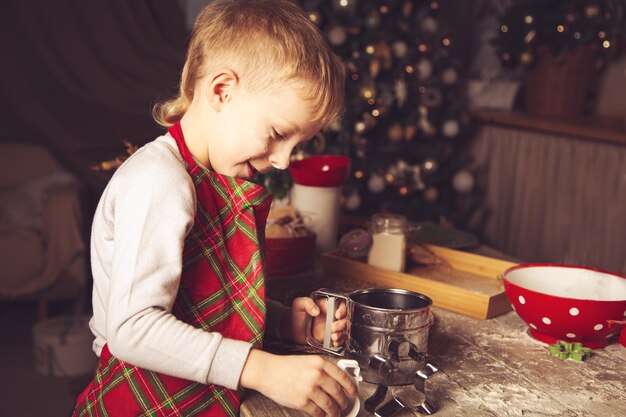 El niño prepara galletas en la cocina. Adornos navideños, tradiciones familiares, comida navideña, vísperas de vacaciones.