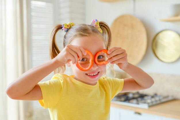 niño preparando comida sana y divirtiéndose sostiene un pimiento frente a sus ojos