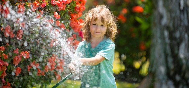 Niño de primavera regando pancarta niño regando flores y plantas en el jardín niño con manguera de agua en la espalda