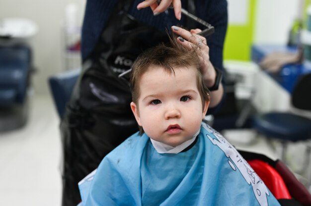 Niño en el primer plano de la peluquería. El primer corte de pelo del niño en la peluquería. Bebé corte de pelo niño.