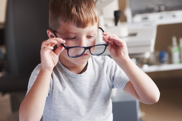 Foto niño probándose sus nuevas gafas en el gabinete del médico.