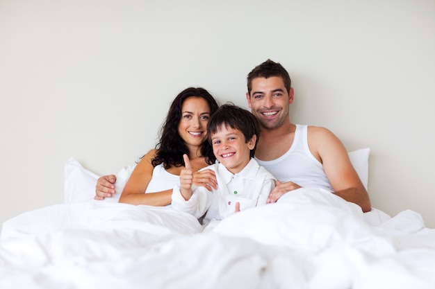 Foto niño con los pulgares arriba y sus padres en la cama