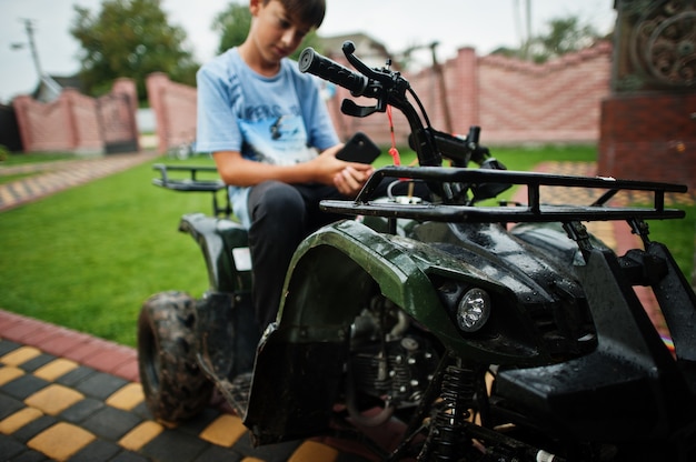 Niño en quad ATV de cuatro ruedas con teléfono móvil.