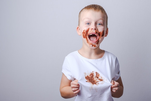 Niño que muestra una mancha sucia de chocolate en una camiseta blanca