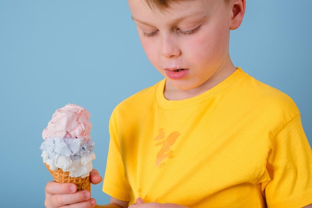 El niño que muestra una mancha sucia de helado en su ropa Él sostiene un cono de helado