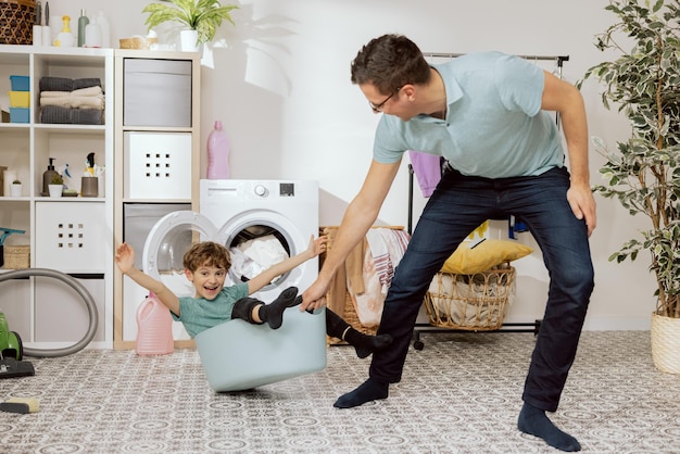 Un niño que se ríe feliz se sienta en un tazón de ropa de plástico, papá tira a su hijo para divertirse engañando