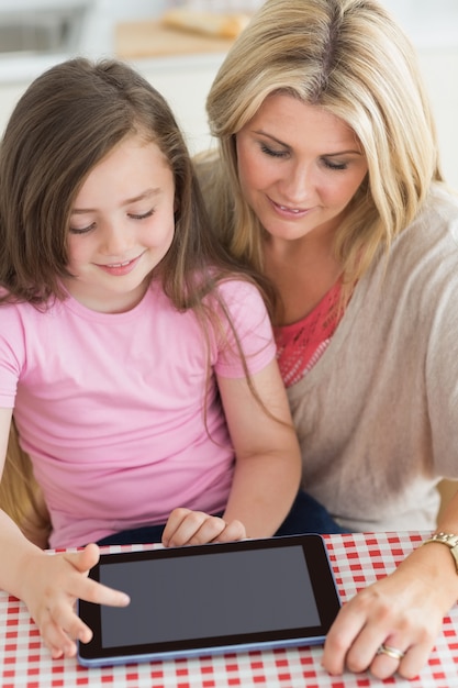 Niño que usa la PC de la tableta con la madre en la cocina