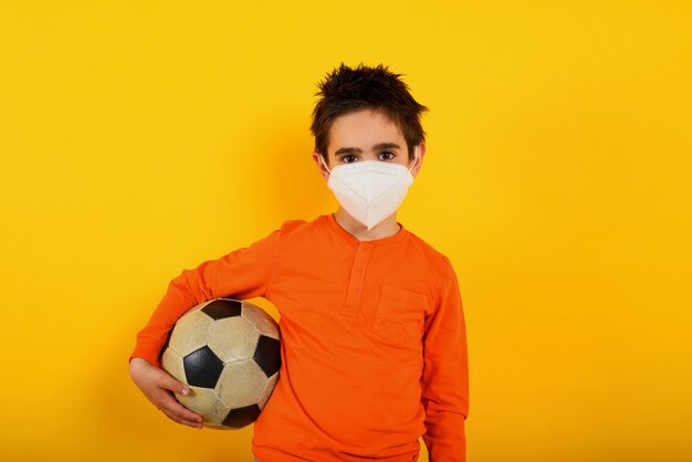 Niño quiere con mascarilla para el coronavirus covid-19 quiere jugar al fútbol en amarillo