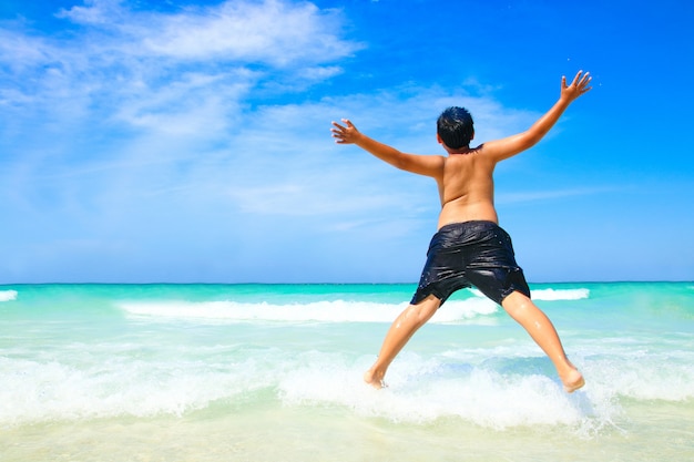 El niño se quitó la camisa y dio un salto. Ven a jugar al hermoso mar, playa de arena blanca, agua clara.