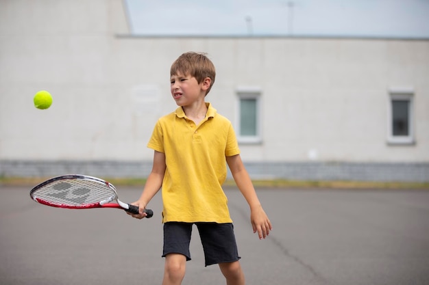 Niño con una raqueta de tenis y una pelota Niño tenista Colegial practica deportes