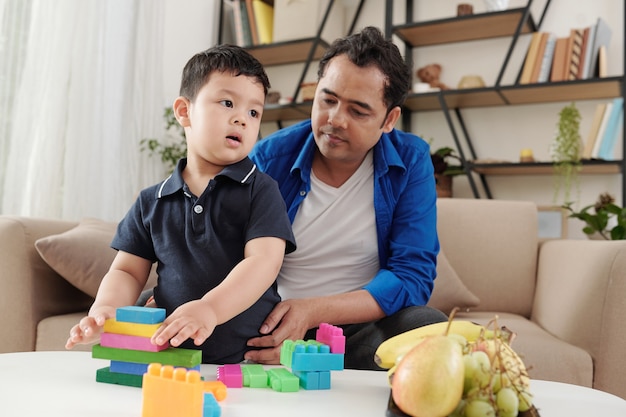 Niño de raza mixta disfrutando jugando con ladrillos de colores con su padre en casa