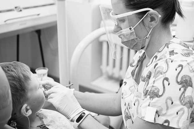 Un niño en la recepción de un dentista en una clínica dental. Odontología infantil, Odontopediatría. Fotografía de estilo retro en blanco y negro. Higiene y salud bucal