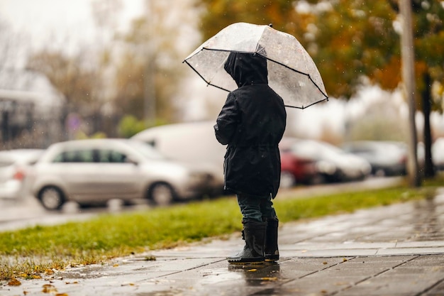 Un niño rechazado está parado en el clima lluvioso solo con su paraguas