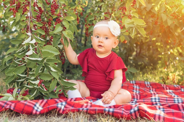Un niño recién nacido de 10 a 12 meses toca las bayas de cerezo que crecen en un arbusto y sonríe feliz mirando a la cámara