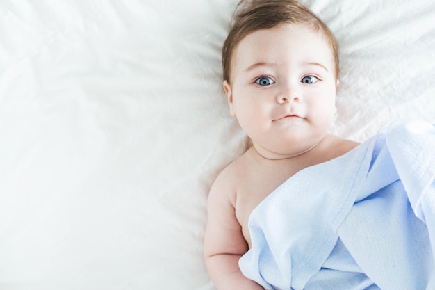 Niño recién nacido desnudo con cubierta en la cama
