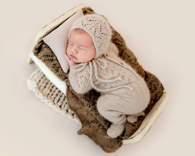 Niño recién nacido durmiendo en una cama pequeña con traje beige tejido. Niño bebé durmiendo una siesta boca abajo durante la sesión de fotos de estudio