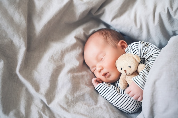 Niño recién nacido niño de una semana durmiendo plácidamente con un lindo juguete de peluche en la cuna en el fondo de tela