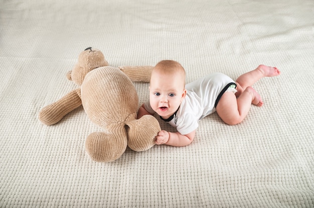 Niño recién nacido con un oso de juguete en el primer plano de la cama y copie el espacio. Bebé gracioso y oso de peluche