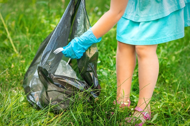 El niño recoge basura plástica de la hierba tirando basura en una bolsa de basura en el parque