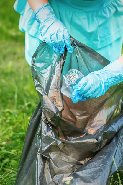 El niño recoge basura plástica de la hierba tirando basura en una bolsa de basura en el parque