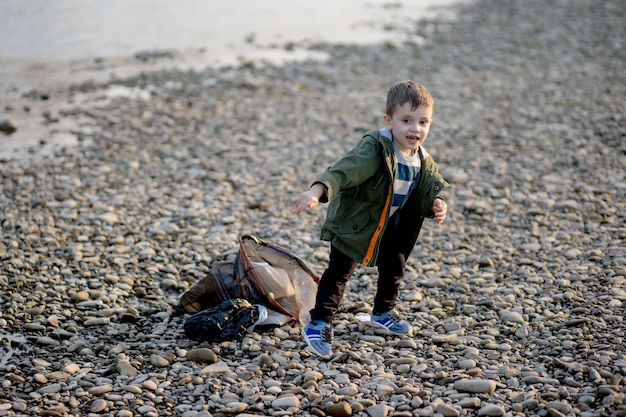 Niño recogiendo basura y botellas de plástico en la playa para tirar a la basura