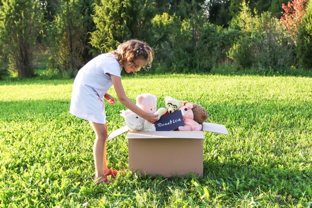 Niño recogiendo juguetes con fines benéficos. Peluches en caja de cartón doantion al aire libre.