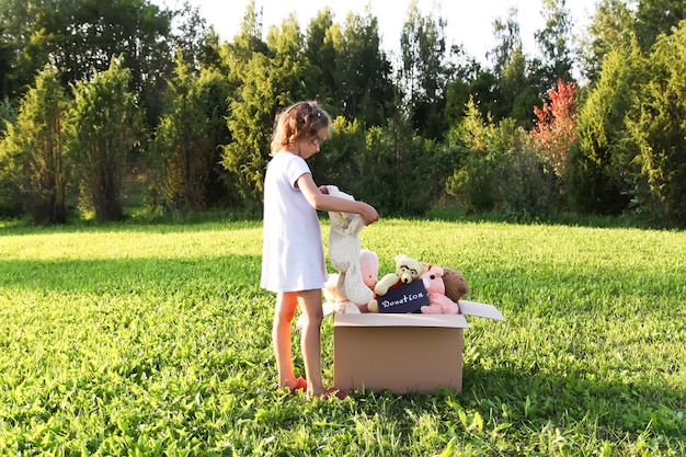 Niño recogiendo juguetes con fines benéficos. Peluches en caja de cartón doantion al aire libre.
