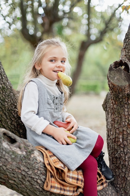 Niño recogiendo manzanas en la granja en otoño. Niña que juega en huerto del manzano. Nutrición saludable.