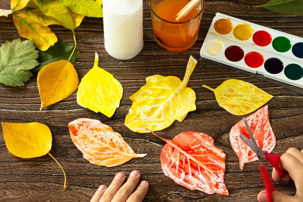 El niño recorta hojas de otoño con una vela y acuarelas Proyecto de arte infantil